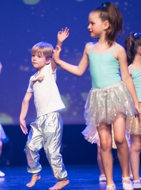 Magic is ND Air 2024 1 Kinderen in kostuum treden betoverend op het podium op, met een jongen in een glimmende broek en een meisje in een glinsterende rok die de schijnwerpers op zich nemen. Het is een scène die rechtstreeks uit de video "Magic is Nd Air 2024" lijkt te komen, waarin elke danspas voelt als pure magie.