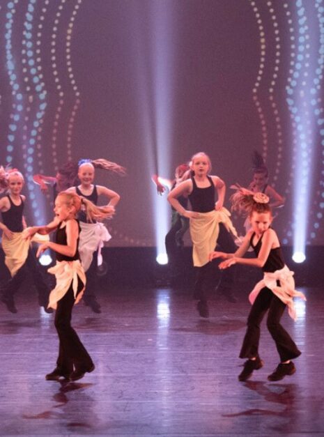 Magic is ND Air 2024 5 Een groep dansers treedt op het podium op, gekleed in zwarte outfits met witte schorten. Felle podiumlichten verlichten hen, met een stippelpatroon op de achtergrond, wat een betoverende scène creëert die doet denken aan Magic is ND Air 2024.