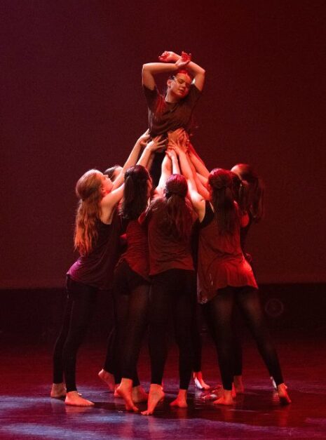 Magic is ND Air 2024 6 Een groep dansers in kastanjebruine outfits tilt een danseres onder rode verlichting boven zich op het podium. Hierdoor ontstaat een tafereel dat aanvoelt als pure magie tijdens de ND Air 2024-showcase.