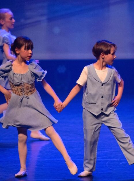 Magic is ND Air 2024 9 Twee jonge kinderen gekleed in lichtblauwe kostuums voeren op het podium een magische dans uit. Ze houden elkaars handen vast, alsof ze samen een spreuk uitspreken.