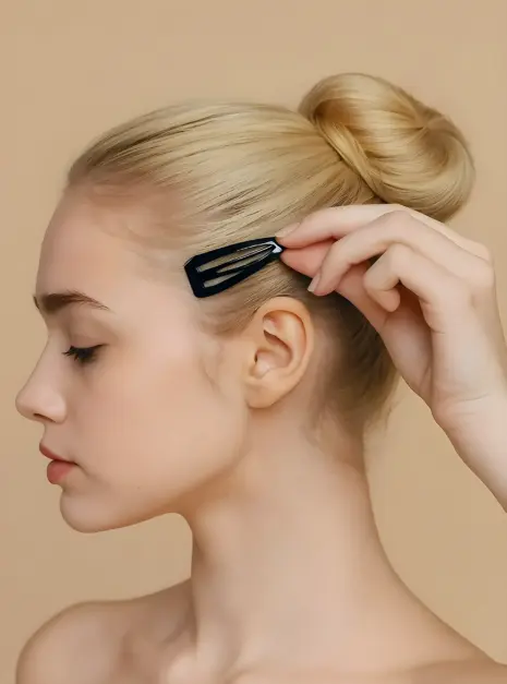 Capezio Snap Clips Een vrouw met blond haar in een knot plaatst Capezio Snap Clips bij haar slaap tegen een beige achtergrond.