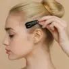 Een vrouw met blond haar in een knot plaatst Capezio Snap Clips bij haar slaap tegen een beige achtergrond.