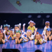 Kinderen in kostuum liggen op het podium met hun handen onder hun kin tijdens de voorstelling N-SPIRATION Dansvoorstelling 2025.