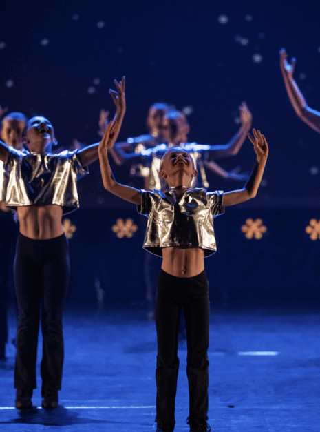 The Greatest Showman - Jazz 1&2 Dansers in metalen topjes voeren gesynchroniseerde bewegingen uit op een schemerig podium in Video: N-SPIRATION Dansvoorstelling 2025.