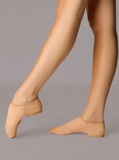 sojz75nud_nude_front-1__66962 Een persoon die bruine jazzdansschoenen zonder veters draagt, staat op één voet terwijl de andere lichtjes omhoog is geheven, tegen een effen achtergrond.