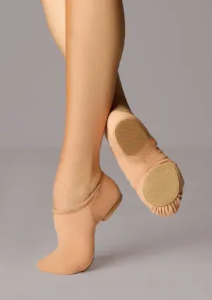 Een persoon die beige jazzschoenen draagt, poseert met één voet in spitsstand en de andere plat op de grond, waarbij de zool en de pasvorm van de schoenen goed te zien zijn tegen een effen achtergrond.