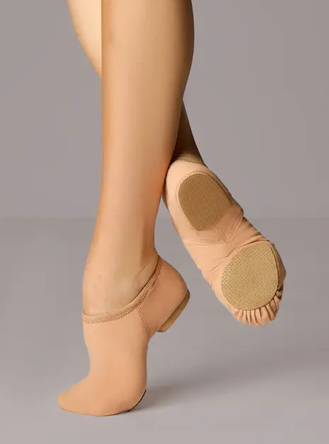 sojz75nud_nude_front-t__26157 Een persoon die beige jazzschoenen draagt, poseert met één voet in spitsstand en de andere plat op de grond, waarbij de zool en de pasvorm van de schoenen goed te zien zijn tegen een effen achtergrond.